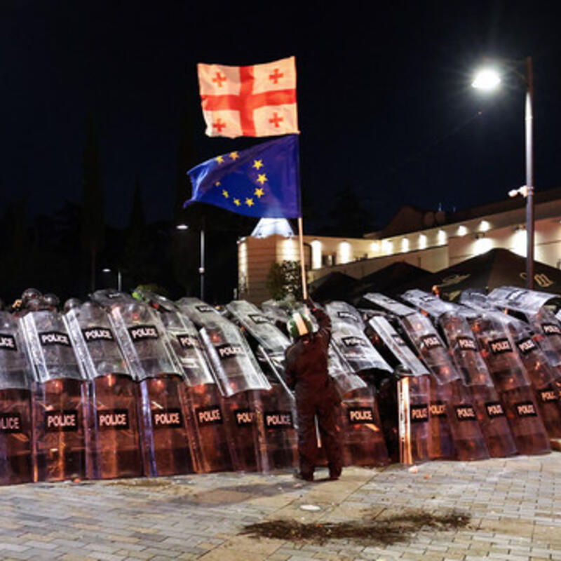 A protester waves a Georgian and a European Union flags in front of riot police